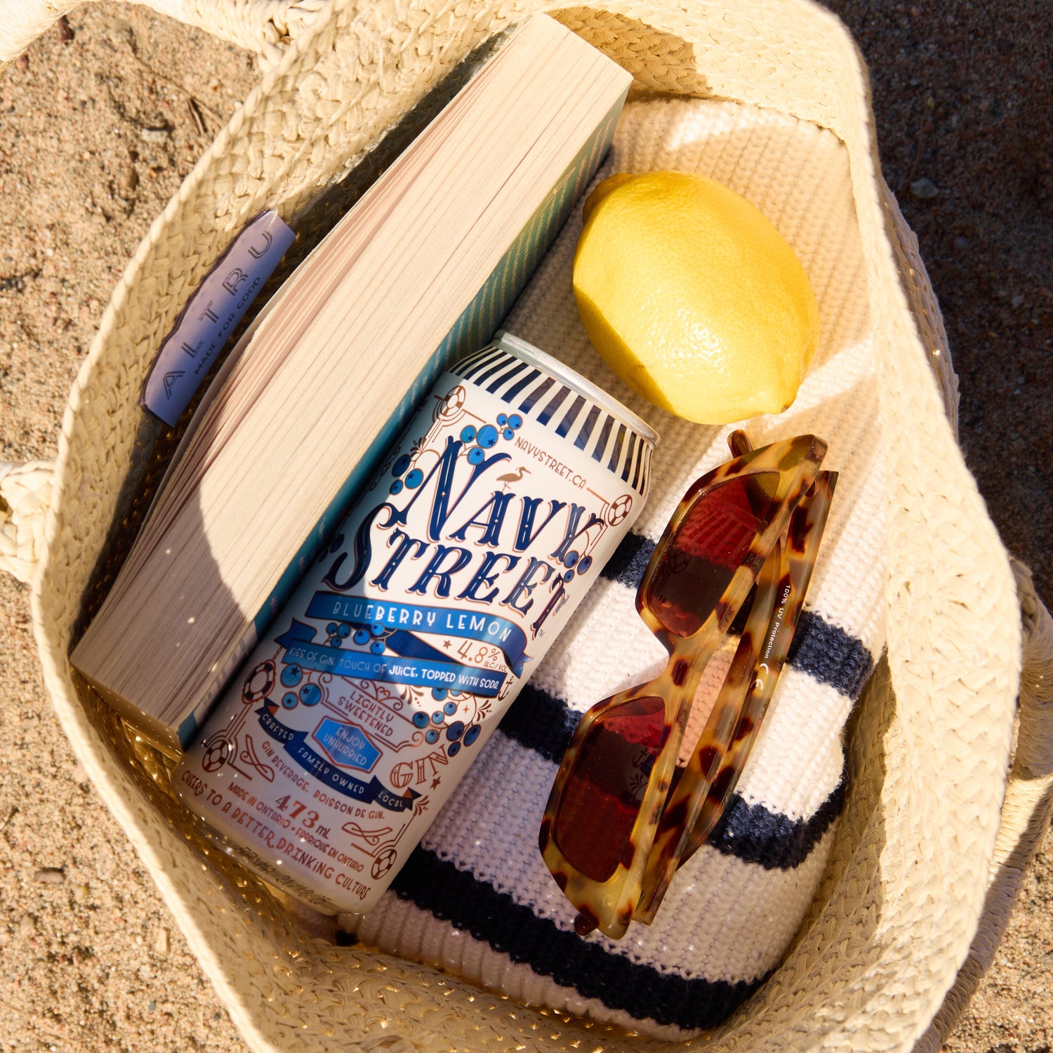 Beach bag with a book, lemon, and sunglasses on sand